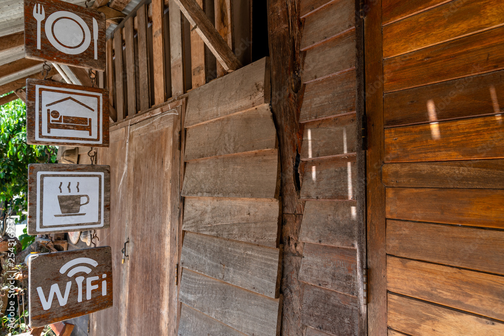 Obraz premium Signs hanging in front of an old wooden homestay indicating food, accommodation, coffee, and free wifi available at Maekampong village in Chiang Mai, Thailand.