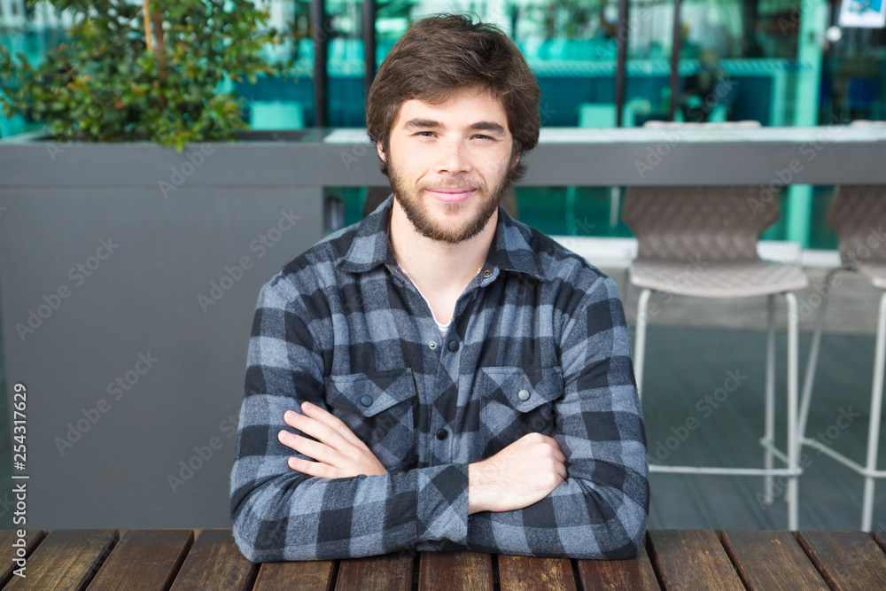 Smiling man sitting at street cafe table with his arms crossed Smiling man sitting at street cafe table with his arms crossed