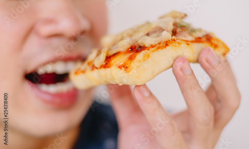 Close up portrait of excited happy hungry young man eating a piece of pizza, focus pizza