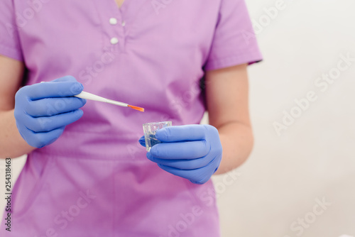 Female hands of a beautician with small glass cup and aplicator