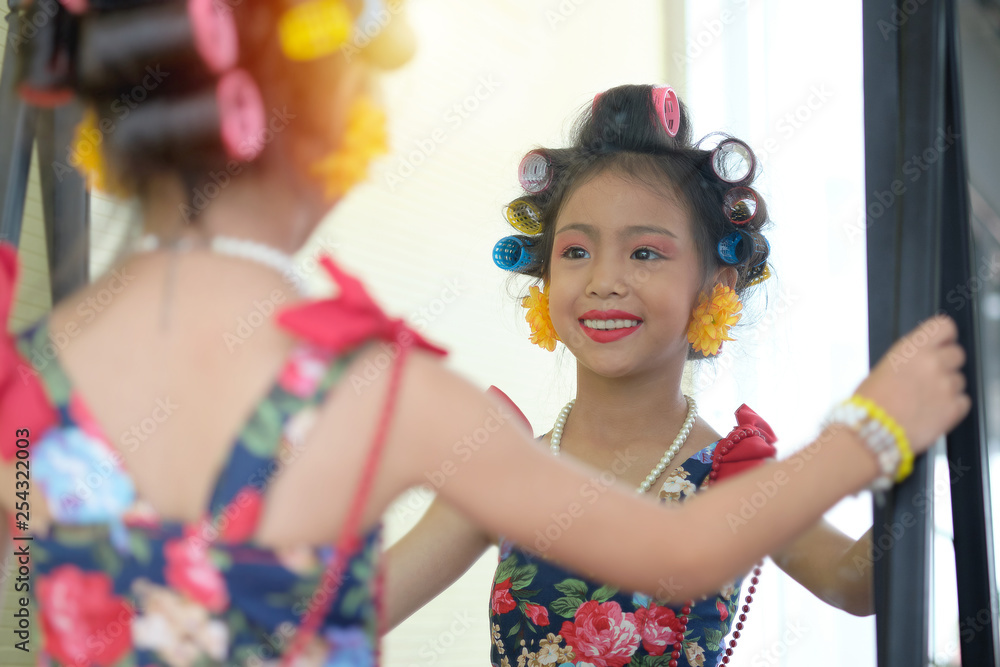 Little girl asian is being happy with dressing in front of the mirror while having a curlers rollers in the hair. Little girl asian is being happy with dressing in front of the mirror while having a curlers rollers in the hair.
