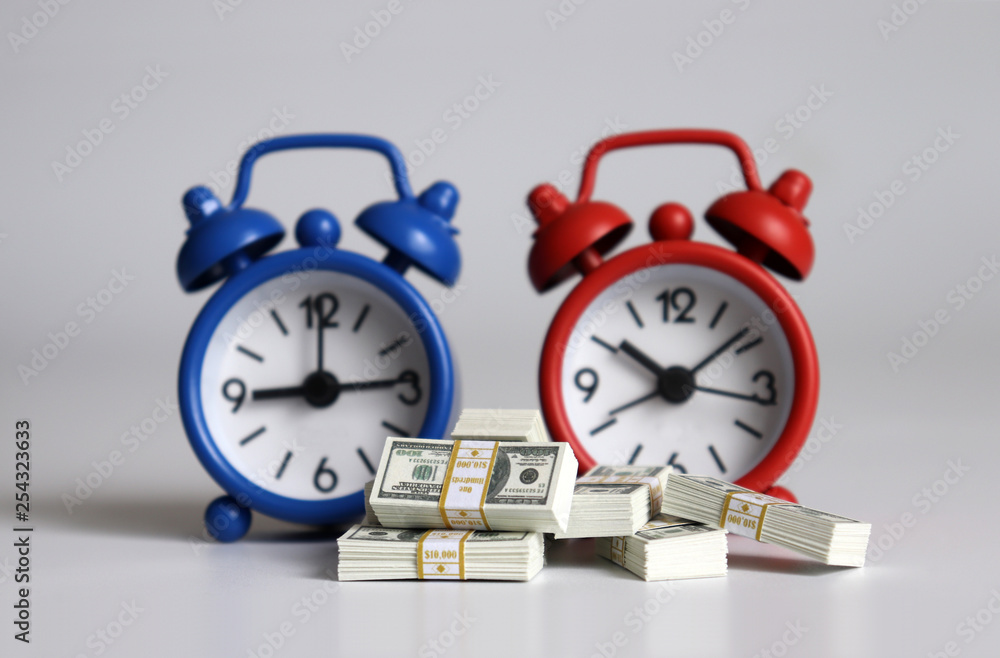 Hundred-dollar bundle in front of two alarm clocks. Hundred-dollar bundle in front of two alarm clocks.