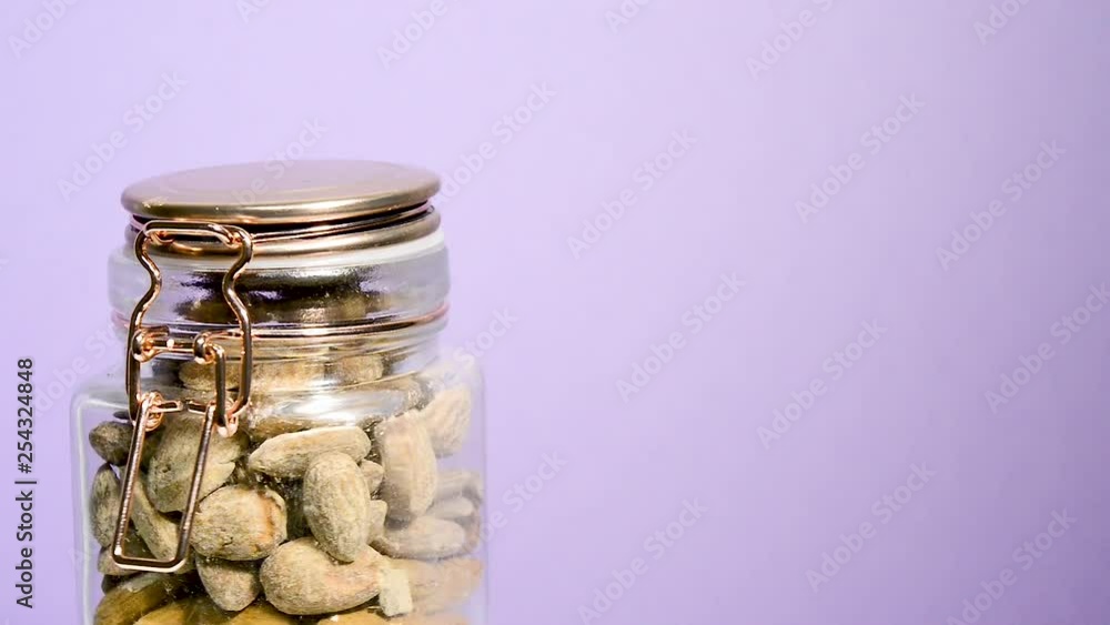 Airtight mason jar rotating with toasted almonds on a neon lilac background. Flat plane. Eye level Airtight mason jar rotating with toasted almonds on a neon lilac background. Flat plane. Eye level