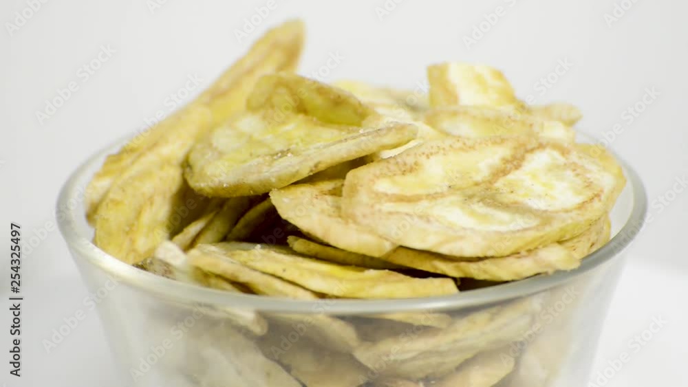 Detail of banana chips in a glass jar rotating on a white background. Flat plane. High angle shot Detail of banana chips in a glass jar rotating on a white background. Flat plane. High angle shot