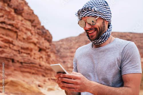 Canvas Print Man with athletic body build is holding his smartphone and looking in it through sunglasses with mirror effect