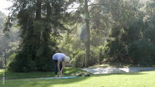 Senior citizen woman does yoga in the park with a sun salutation.