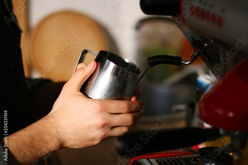 hand with cup of coffee and machine, barista steaming the milk