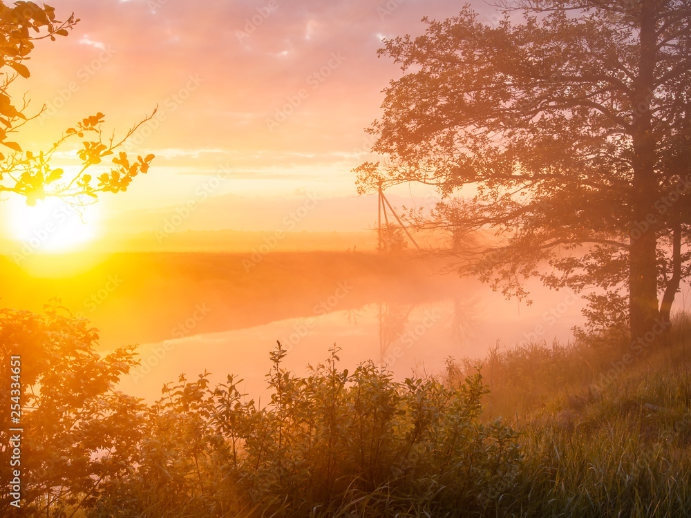 Misty morning at the riverbank in summer. Rising sun shining though the fog Misty morning at the riverbank in summer. Rising sun shining though the fog