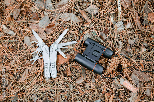 multi tool knife and binoculars on the ground covered with pine needles photo