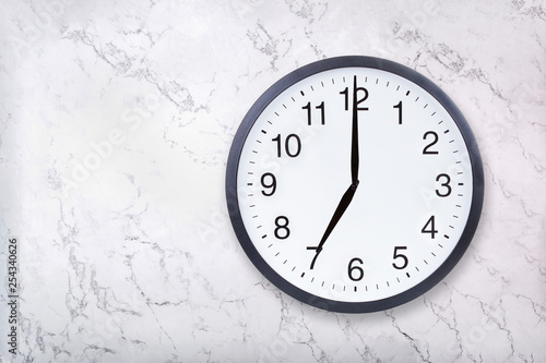 Wall clock show seven o'clock on white marble texture. Office clock show 7pm or 7am on marble background