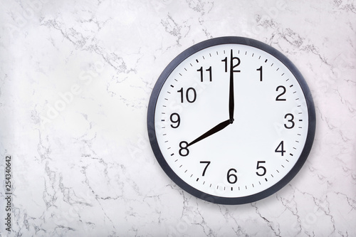 Wall clock show eight o'clock on white marble texture. Office clock show 8pm or 8am on marble background