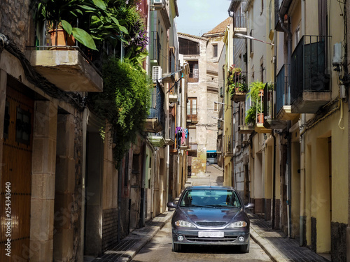 Modern car on a narrow street in a residential area in Tarrega (Catalonia, Spain). The contrast between the future and the past, the old Gothic street with floral balconies and modern transport on it