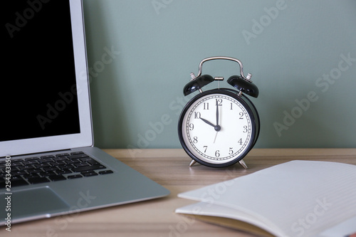 Laptop, clock and notebook on table