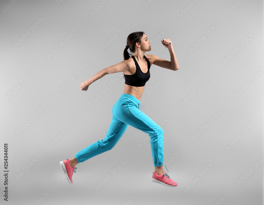 Sporty young woman running against light background