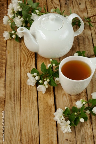 Jasmine tea.  tea with jasmine extract, white teapot and white mug with tea, blooming sprigs of jasmine on a wooden brown background.Herbal organic wholesome tea