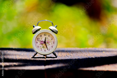 The clock is placed on the old wood in the daytime and the background is blurred.