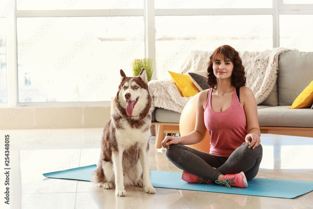 Young woman with her cute dog practicing yoga at home