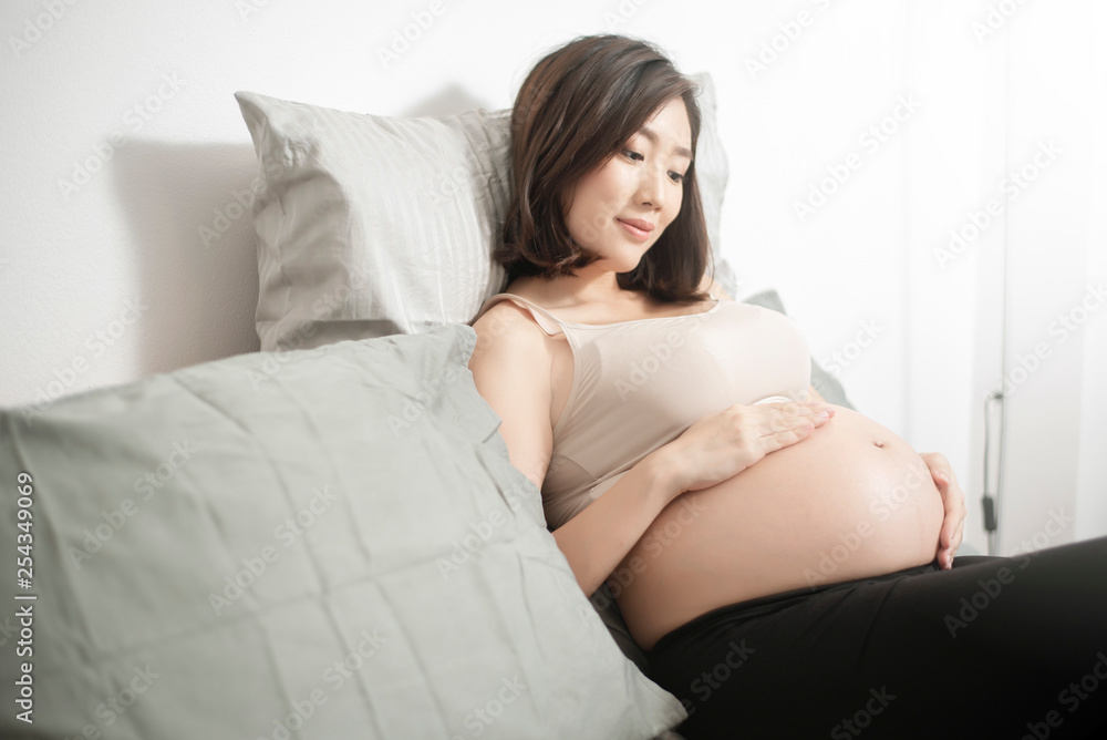 Beautiful asian pregnant woman lying on her bed, touching big belly Beautiful asian pregnant woman lying on her bed, touching big belly