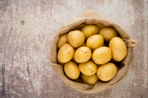 Sack of fresh raw potatoes on wooden background, top view.