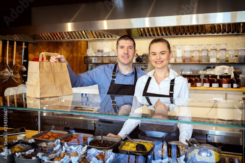 Business restaurant owners smiling behind counter holding paper bag with food order for home delivery