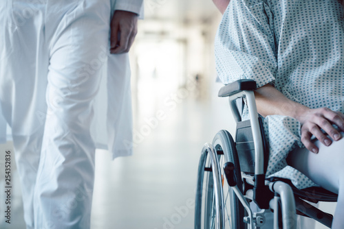 Doctor and nurse pushing wheelchair with patient in hospital