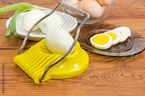 Whole and sliced eggs and egg slicer on rustic table photo