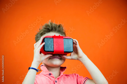 funny boy in virtual reality glasses playing smartphone on orange background