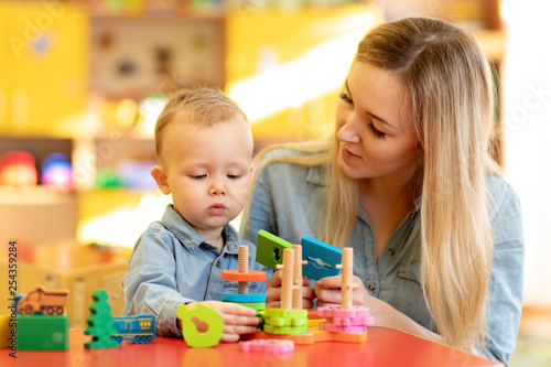 Baby minder playing with kid in nursery. Developmental toys for preschool.