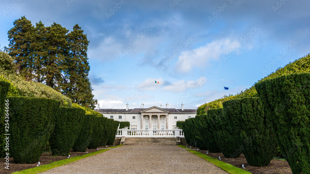 Front view of the official residence of the President of Ireland and gardens, built in 1751, with the Irish and the EU flag on the roof, under a dramatic sky, as seen from Phoenix Park, Dublin.