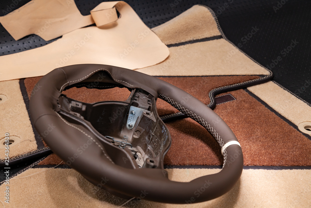 Leather steering wheel brown color in the process of stitching with a bright contrast seam and white central point on the top in the workshop for the repair of car interiors and tuning design Leather steering wheel brown color in the process of stitching with a bright contrast seam and white central point on the top in the workshop for the repair of car interiors and tuning design