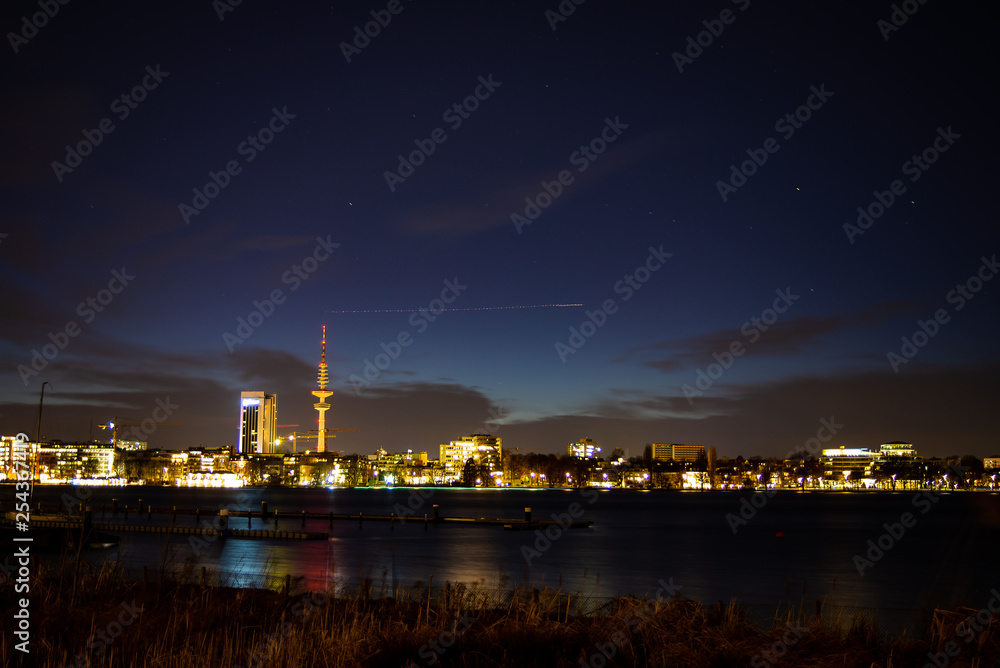 A airplane's lights approaching Hamburg airport form a streak above downtown Hamburg at night