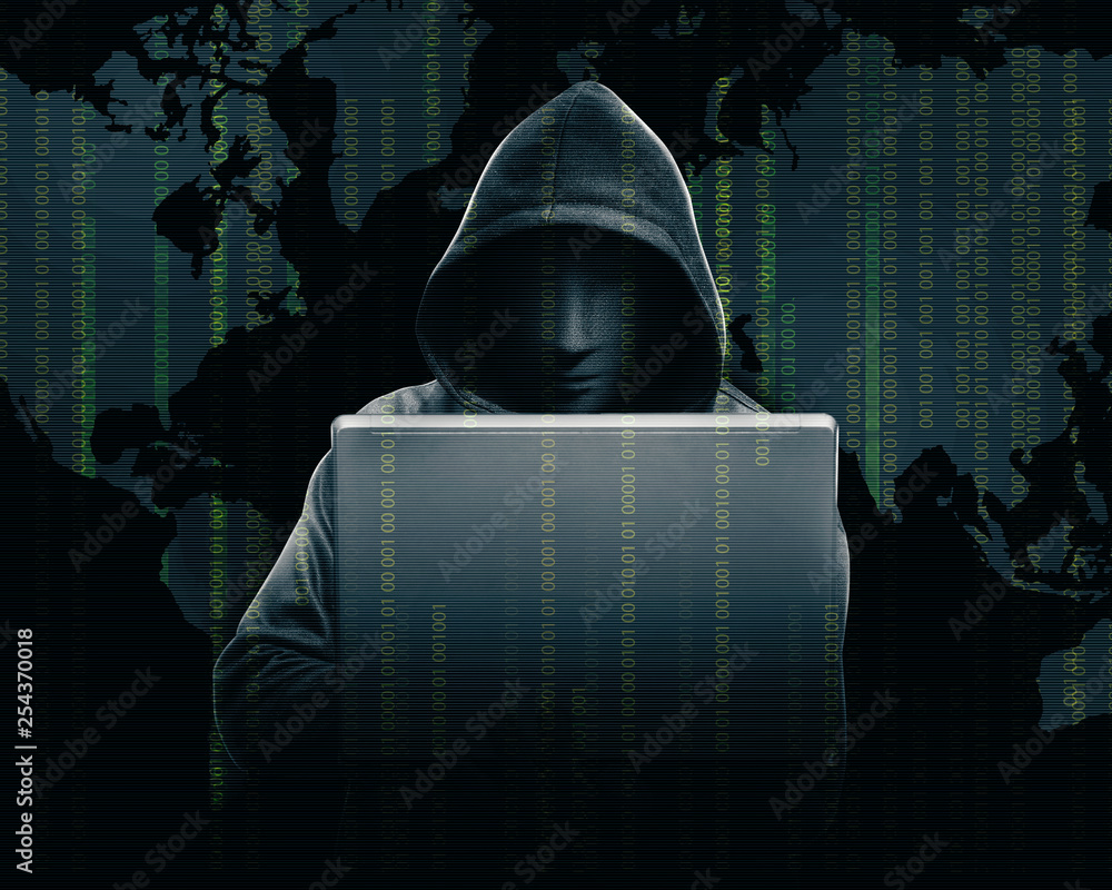 Hacker in black hoodie holding laptop with his hand and world map with ...