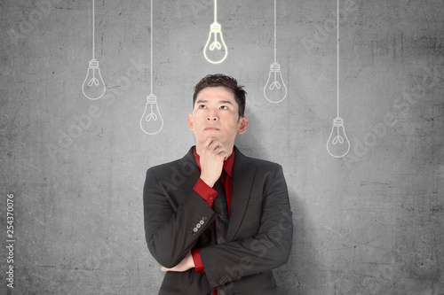 Young asian businessman thinking for new innovative idea with bright light bulbs hanging