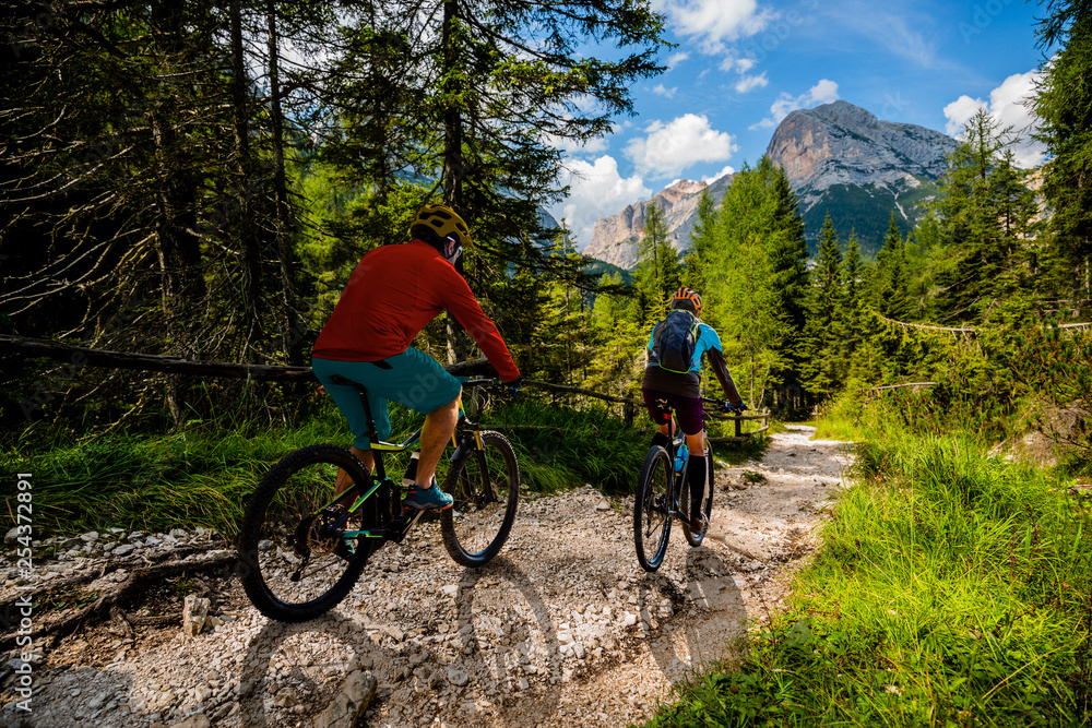 Fototapeta premium Cycling woman and man riding on bikes in Dolomites mountains andscape. Couple cycling MTB enduro trail track. Outdoor sport activity.