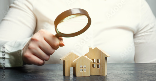 A woman is holding a magnifying glass over a wooden houses. Real estate appraiser. Property valuation / appraisal. Find a house. Search for housing. Real estate market analysis. Selective focus photo
