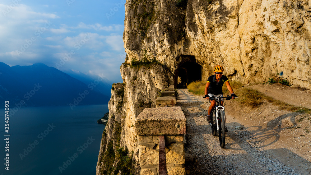 Mountain biking woman at sunrise over Lake Garda on path Sentiero della Ponale, Riva del Garda, Italy