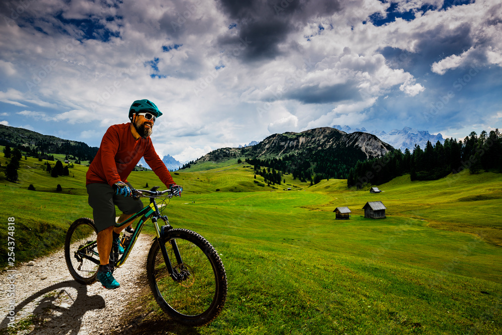Fototapeta premium Tourist cycling in Cortina d'Ampezzo, stunning rocky mountains on the background. Man riding MTB enduro flow trail. South Tyrol province of Italy, Dolomites.