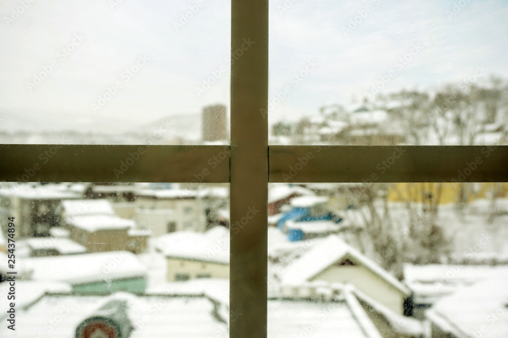Fototapeta premium Closeup wooden frame of window and glass with blurry outside view of snow capped city and winter blue sky background.