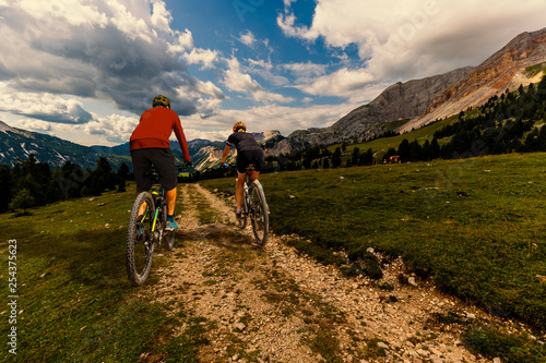 Cycling woman and man riding on bikes in Dolomites mountains andscape. Couple cycling MTB enduro trail track. Outdoor sport activity.