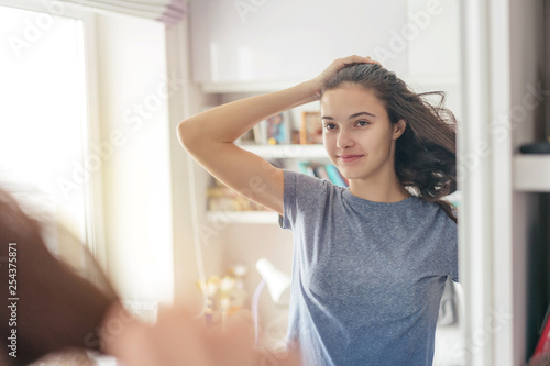 young girl straightens her long hair  reflected in the mirror