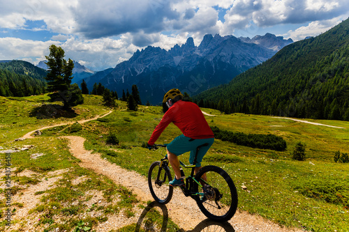Tourist cycling in Cortina d Ampezzo  stunning rocky mountains on the background. Man riding MTB enduro flow trail. South Tyrol province of Italy  Dolomites.