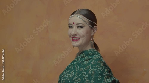 Portrait of fashionable female glancing at camera and charmingly smiling. Close-up of elegant woman in traditional sari, jewelry with bindi point and bright makeup looking confident and enigmatic.