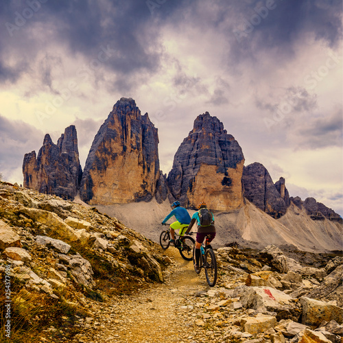 Cycling woman and man riding on bikes in Dolomites mountains andscape. Couple cycling MTB enduro trail track. Outdoor sport activity.