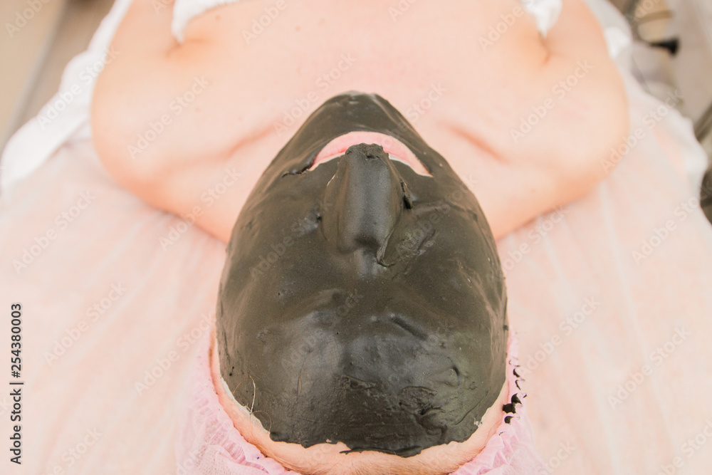 Naklejka premium Woman in the spa salon, It makes a face mask, facial rejuvenation procedure, spa treatments. Visit a beautician, Cosmetology. Selective focus
