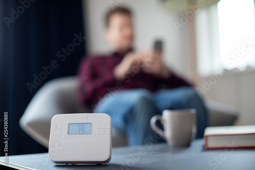 Man Controlling Central Heating Smart Meter Using App On Mobile Phone