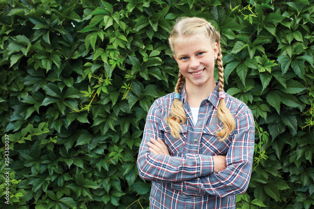 A teenage girl is smiling in the summer garden against a background of a wall of green leaves. Portrait A teenage girl is smiling in the summer garden against a background of a wall of green leaves. Portrait