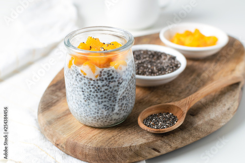 Chia pudding in glass jar with almond milk and mango on white background