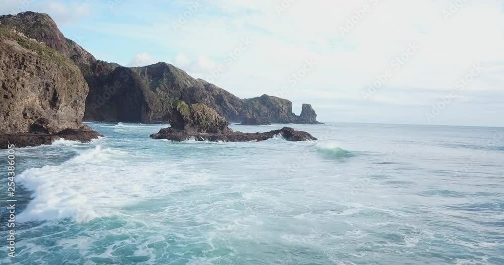 Drone shot of Bethells Beach, New Zealand with ocean waves crashing on the singular cliffs, near the sandy beach, on a sunny day Drone shot of Bethells Beach, New Zealand with ocean waves crashing on the singular cliffs, near the sandy beach, on a sunny day
