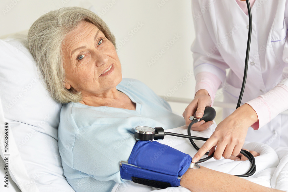 Obraz premium Portrait of senior woman in hospital with caring doctor measuring pressure