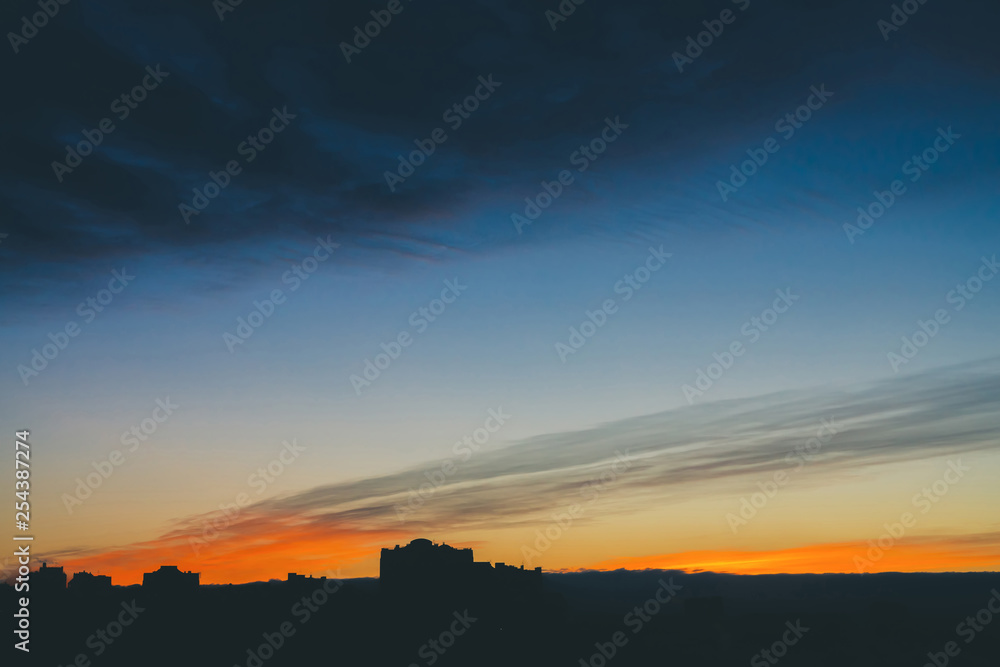 Cityscape with wonderful varicolored vivid dawn. Amazing dramatic blue cloud sky above dark silhouettes of city building roofs. Atmospheric background of orange sunrise in overcast weather. Copy space Cityscape with wonderful varicolored vivid dawn. Amazing dramatic blue cloud sky above dark silhouettes of city building roofs. Atmospheric background of orange sunrise in overcast weather. Copy space